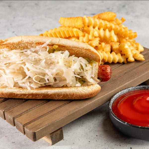 Stewart's Drive-In hot dog with sauerkraut and relish, waffle fries, and ketchup on a wooden board.